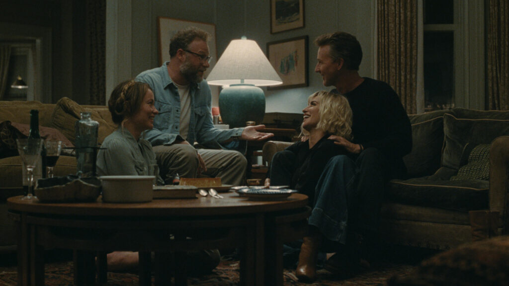 Two couples sit together in a living room during a dinner party in The Invite