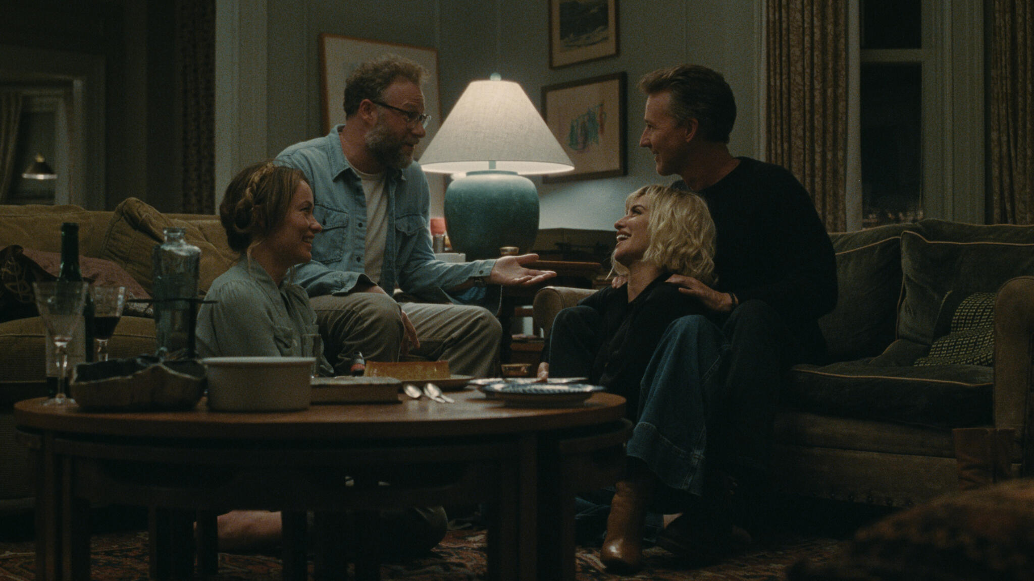 Two couples sit together in a living room during a dinner party in The Invite